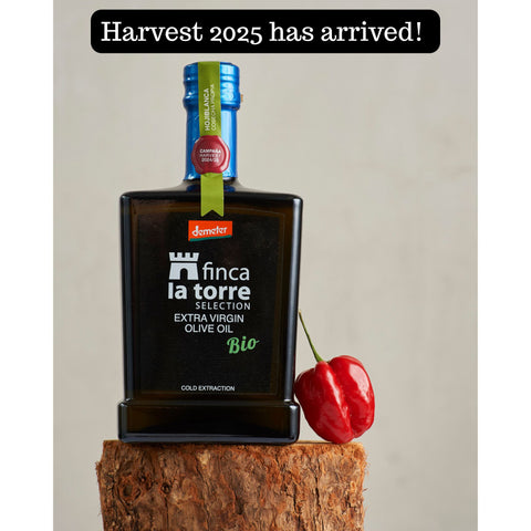 Bottle of Finca La Torre Bio Extra Virgin Olive Oil Harvest 2025 displayed on a wooden stump beside a red pepper, with a banner reading “Harvest 2025 has arrived.”